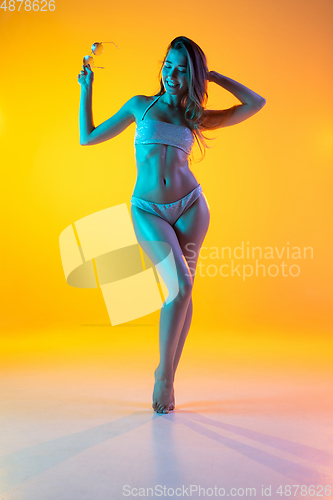 Image of Fashion portrait of seductive girl in stylish swimwear posing on a bright yellow background. Summertime, beach season