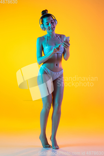 Image of Fashion portrait of seductive girl in stylish swimwear posing on a bright yellow background. Summertime, beach season