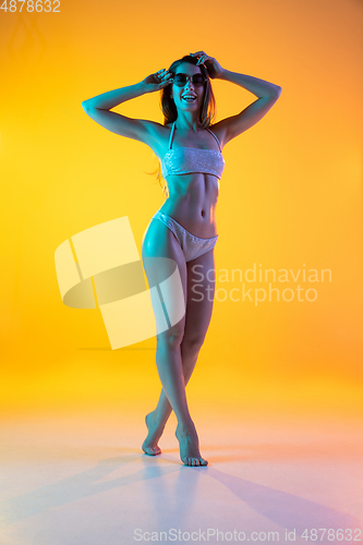 Image of Fashion portrait of seductive girl in stylish swimwear posing on a bright yellow background. Summertime, beach season