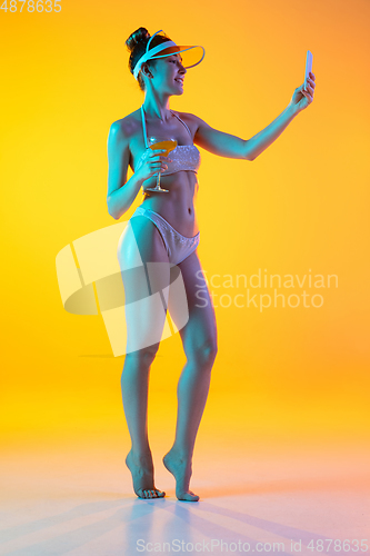 Image of Fashion portrait of seductive girl in stylish swimwear posing on a bright yellow background. Summertime, beach season