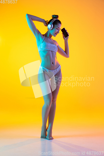 Image of Fashion portrait of seductive girl in stylish swimwear posing on a bright yellow background. Summertime, beach season