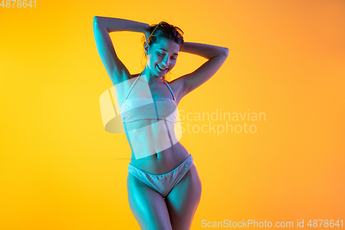 Image of Fashion portrait of seductive girl in stylish swimwear posing on a bright yellow background. Summertime, beach season