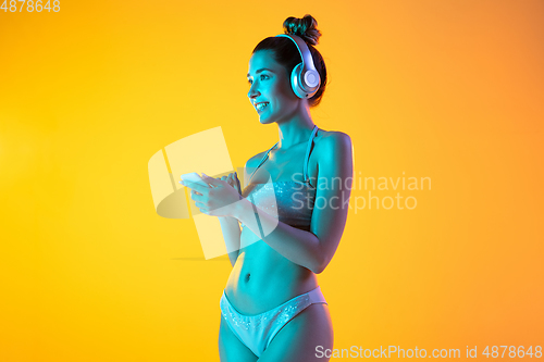 Image of Fashion portrait of seductive girl in stylish swimwear posing on a bright yellow background. Summertime, beach season