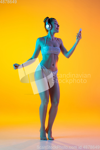 Image of Fashion portrait of seductive girl in stylish swimwear posing on a bright yellow background. Summertime, beach season