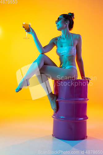 Image of Fashion portrait of seductive girl in stylish swimwear posing on a bright yellow background. Summertime, beach season