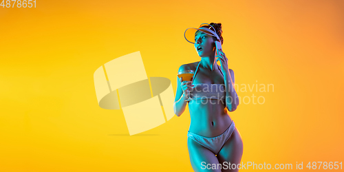 Image of Fashion portrait of seductive girl in stylish swimwear posing on a bright yellow background. Summertime, beach season