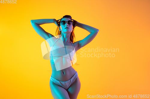 Image of Fashion portrait of seductive girl in stylish swimwear posing on a bright yellow background. Summertime, beach season