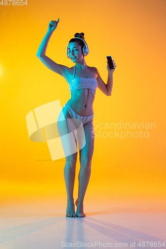 Image of Fashion portrait of seductive girl in stylish swimwear posing on a bright yellow background. Summertime, beach season