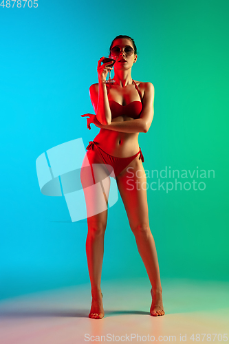 Image of Fashion portrait of seductive girl in stylish swimwear posing on a bright gradient background. Summertime, beach season