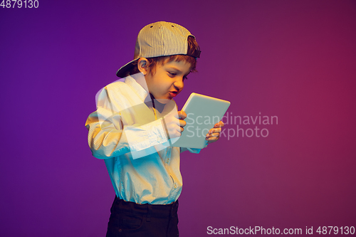 Image of Caucasian boy\'s portrait on gradient studio background in neon light. Beautiful curly model. Concept of human emotions, facial expression, sales, ad, tech