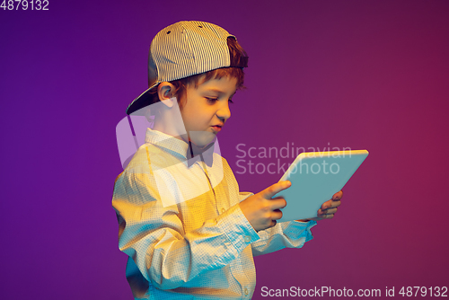 Image of Caucasian boy\'s portrait on gradient studio background in neon light. Beautiful curly model. Concept of human emotions, facial expression, sales, ad, tech