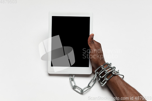 Image of Close up of human hand using tablet with blank black screen. Tied with chain, addiction