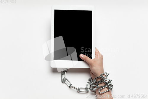 Image of Close up of human hand using tablet with blank black screen. Tied with chain, addiction