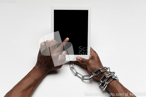 Image of Close up of human hand using tablet with blank black screen. Tied with chain, addiction