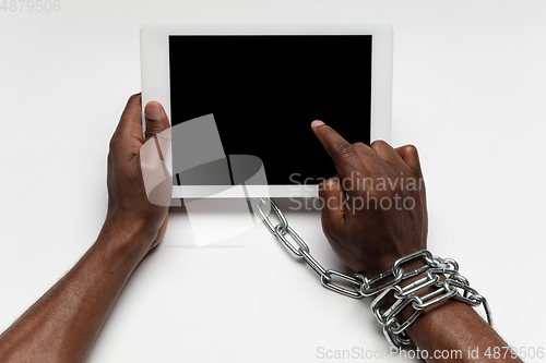 Image of Close up of human hand using tablet with blank black screen. Tied with chain, addiction