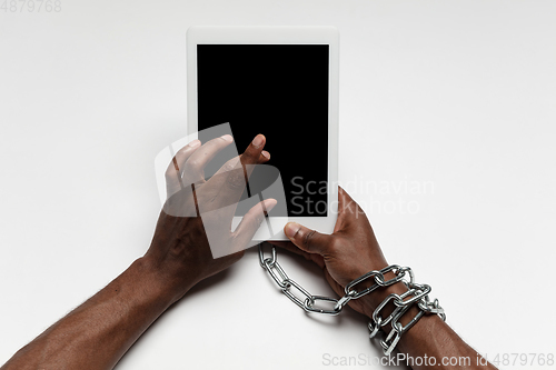 Image of Close up of human hand using tablet with blank black screen. Tied with chain, addiction