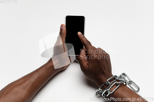 Image of Close up of human hand using smartphone with blank black screen. Tied with chain, addiction