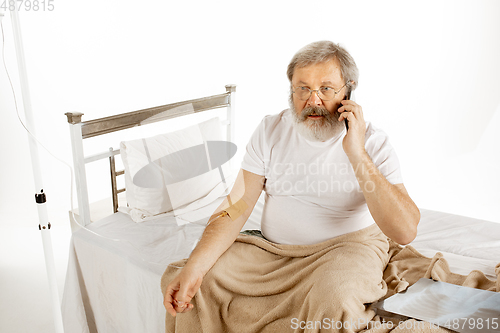 Image of Elderly old man recovering in a hospital bed isolated on white