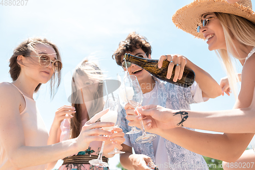 Image of Seasonal feast at beach resort. Group of friends celebrating, resting, having fun on the beach in sunny summer day