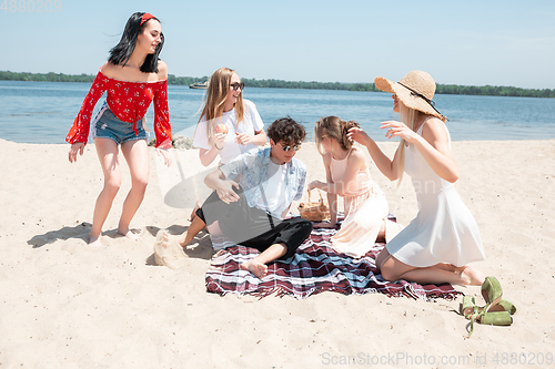 Image of Seasonal feast at beach resort. Group of friends celebrating, resting, having fun on the beach in sunny summer day