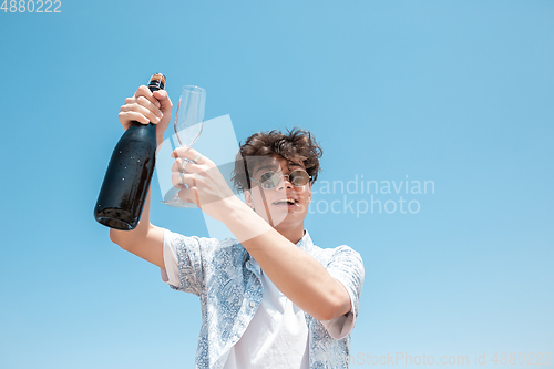 Image of Seasonal feast at beach resort. Happy stylish boy celebrating, resting, having fun on the beach in sunny summer day