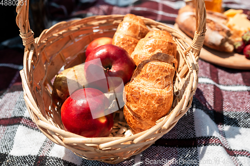 Image of Picnic bread, croissant basket with fruit on cloth with bright sunlight