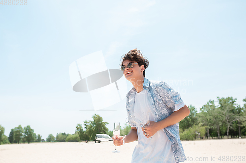 Image of Seasonal feast at beach resort. Happy stylish boy celebrating, resting, having fun on the beach in sunny summer day