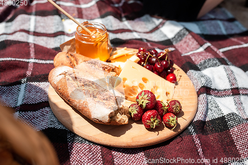 Image of Picnic bread, croissant basket with fruit on cloth with bright sunlight