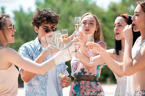 Image of Seasonal feast at beach resort. Group of friends celebrating, resting, having fun on the beach in sunny summer day