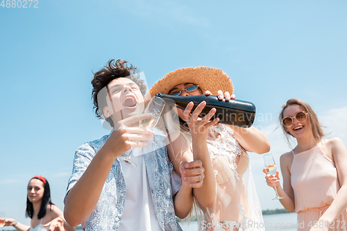 Image of Seasonal feast at beach resort. Group of friends celebrating, resting, having fun on the beach in sunny summer day