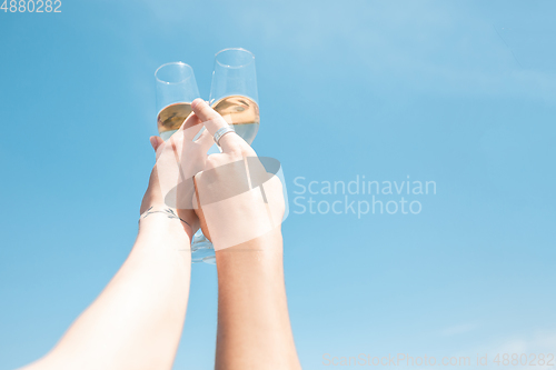 Image of Seasonal feast at beach resort. Close up hands of friends celebrating, resting, having fun, clinking glasses on sky background