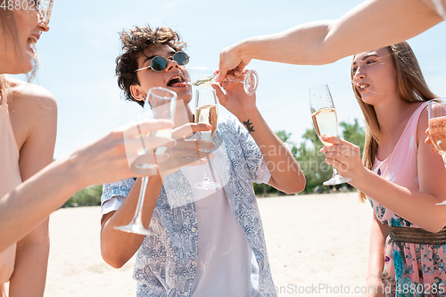 Image of Seasonal feast at beach resort. Group of friends celebrating, resting, having fun on the beach in sunny summer day