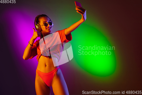 Image of Beautiful seductive girl in fashionable swimsuit on disco bicolored neon studio background in neon light. Summer, resort, fashion and weekend concept