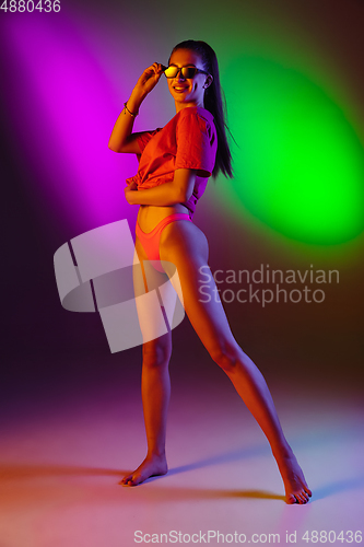 Image of Beautiful seductive girl in fashionable swimsuit on disco bicolored neon studio background in neon light. Summer, resort, fashion and weekend concept