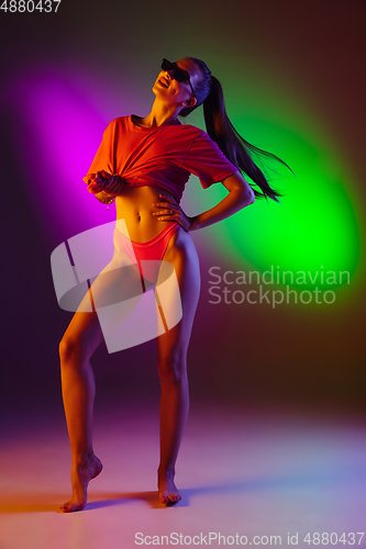 Image of Beautiful seductive girl in fashionable swimsuit on disco bicolored neon studio background in neon light. Summer, resort, fashion and weekend concept