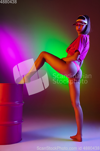 Image of Beautiful seductive girl in fashionable swimsuit on disco bicolored neon studio background in neon light. Summer, resort, fashion and weekend concept