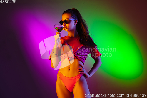 Image of Beautiful seductive girl in fashionable swimsuit on disco bicolored neon studio background in neon light. Summer, resort, fashion and weekend concept