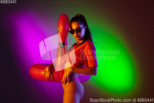 Image of Beautiful seductive girl in fashionable swimsuit on disco bicolored neon studio background in neon light. Summer, resort, fashion and weekend concept