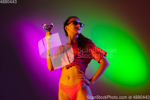 Image of Beautiful seductive girl in fashionable swimsuit on disco bicolored neon studio background in neon light. Summer, resort, fashion and weekend concept