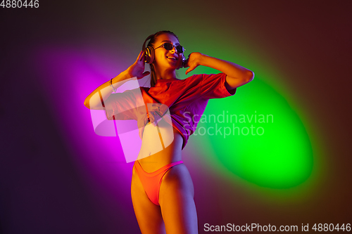 Image of Beautiful seductive girl in fashionable swimsuit on disco bicolored neon studio background in neon light. Summer, resort, fashion and weekend concept