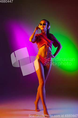 Image of Beautiful seductive girl in fashionable swimsuit on disco bicolored neon studio background in neon light. Summer, resort, fashion and weekend concept