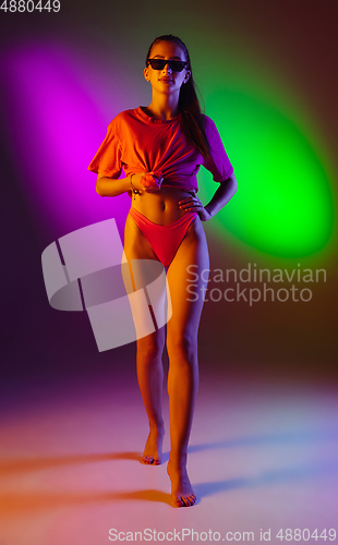 Image of Beautiful seductive girl in fashionable swimsuit on disco bicolored neon studio background in neon light. Summer, resort, fashion and weekend concept