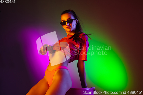 Image of Beautiful seductive girl in fashionable swimsuit on disco bicolored neon studio background in neon light. Summer, resort, fashion and weekend concept