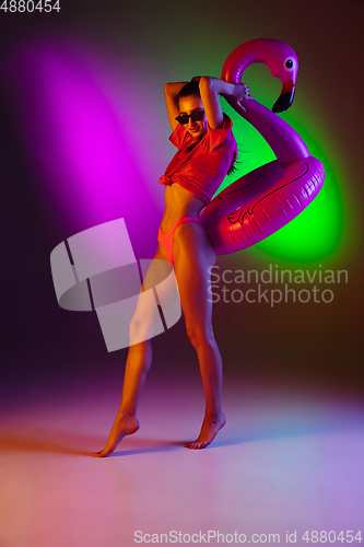 Image of Beautiful seductive girl in fashionable swimsuit on disco bicolored neon studio background in neon light. Summer, resort, fashion and weekend concept