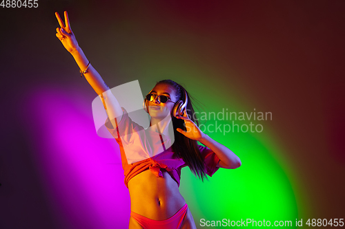 Image of Beautiful seductive girl in fashionable swimsuit on disco bicolored neon studio background in neon light. Summer, resort, fashion and weekend concept