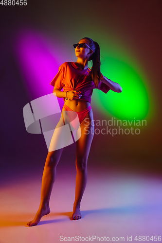 Image of Beautiful seductive girl in fashionable swimsuit on disco bicolored neon studio background in neon light. Summer, resort, fashion and weekend concept