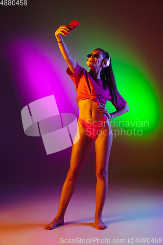 Image of Beautiful seductive girl in fashionable swimsuit on disco bicolored neon studio background in neon light. Summer, resort, fashion and weekend concept