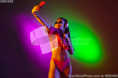 Image of Beautiful seductive girl in fashionable swimsuit on disco bicolored neon studio background in neon light. Summer, resort, fashion and weekend concept