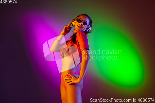 Image of Beautiful seductive girl in fashionable swimsuit on disco bicolored neon studio background in neon light. Summer, resort, fashion and weekend concept