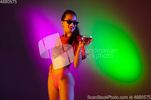 Image of Beautiful seductive girl in fashionable swimsuit on disco bicolored neon studio background in neon light. Summer, resort, fashion and weekend concept